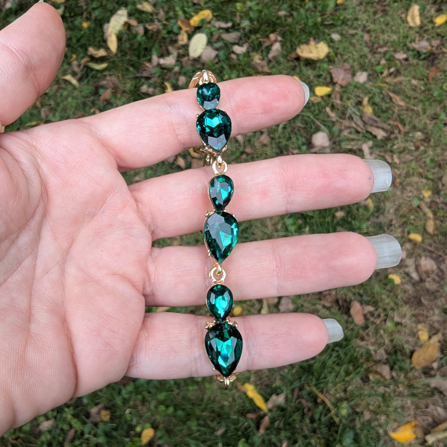 Hand holding a emerald green gemstone necklace against a grassy background