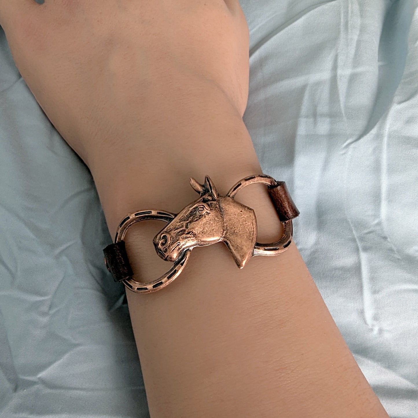 Copper horse head and bit bracelet on a wrist against a light fabric background
