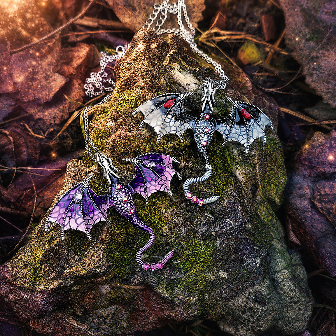 Dragon-shaped pendants on a textured stone surface with leaves in the background.  Dragon fantasy jewelry
