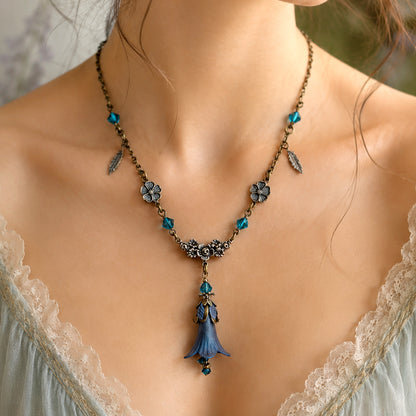 A close-up of a woman wearing a fairy-style bronze necklace with turquoise beads, floral charms, feather details, and a blue bell flower shaped pendant.