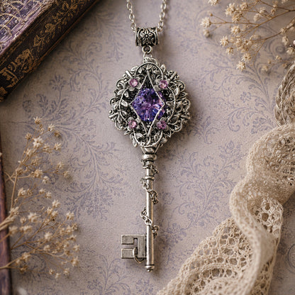 Decorative key-shaped pendant with purple gemstone on a textured surface with lace and flowers.  Fairycore Silver Key Necklace with Swarovski Crystal – Fantasy Floral Jewelry