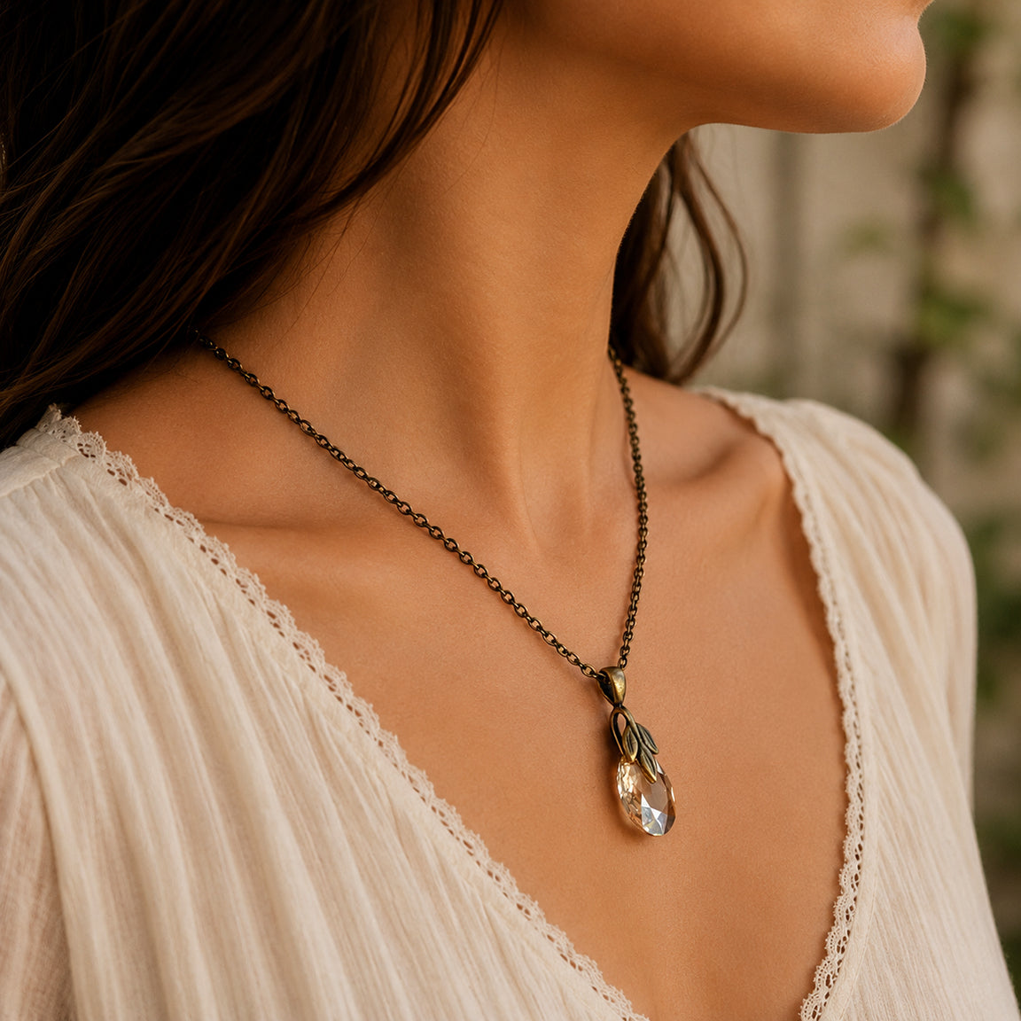 Necklace with a crystal pendant and brass leaf bail worn by a person in a white top, blurred background