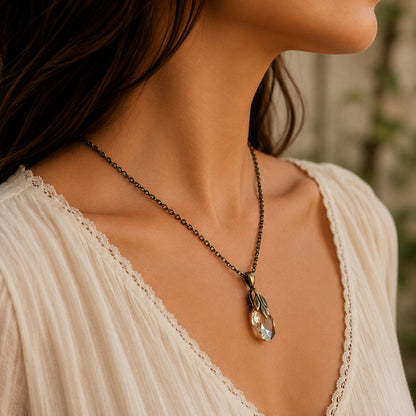 Necklace with a crystal pendant and brass leaf bail worn by a person in a white top, blurred background