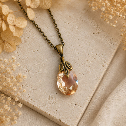 Necklace with a teardrop-shaped Swarovski crystal pendant on a textured surface with dried flowers.