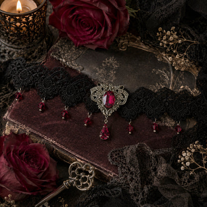 Gothic-style lace choker jewelry with red Swarovski gemstones on a dark surface with roses and a candle