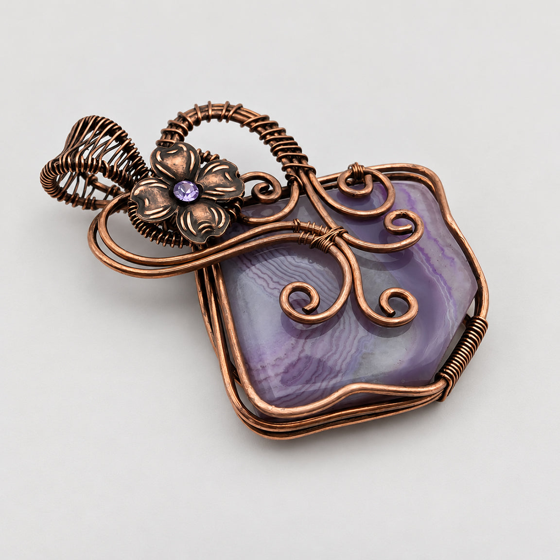 Wire wrapped purple solar agate fairy pendant with flower on neutral surface
