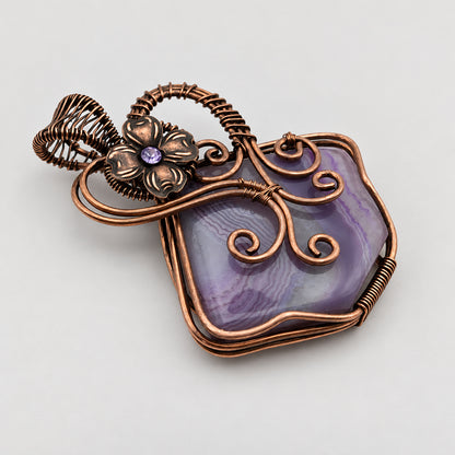 Wire wrapped purple solar agate fairy pendant with flower on neutral surface