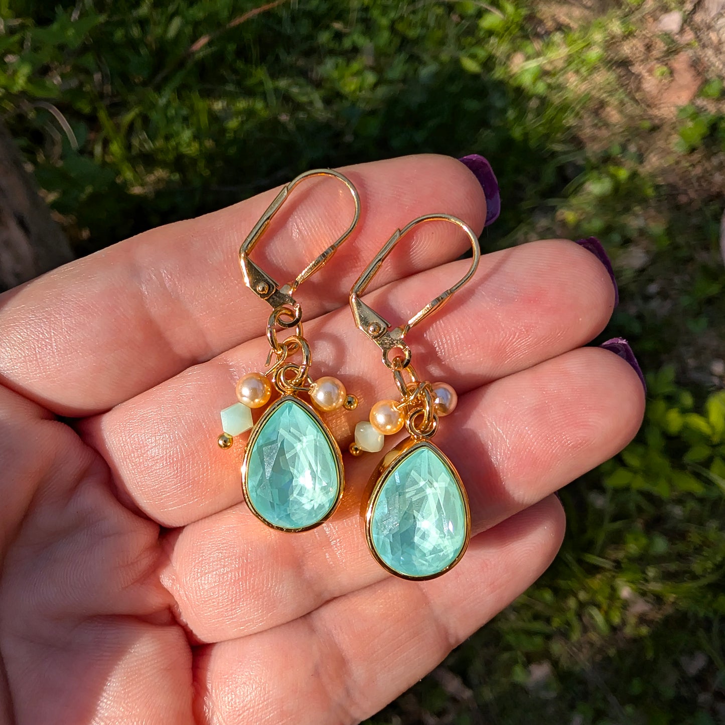Gold earrings with mint green Swarovski stones held in a hand against a natural background