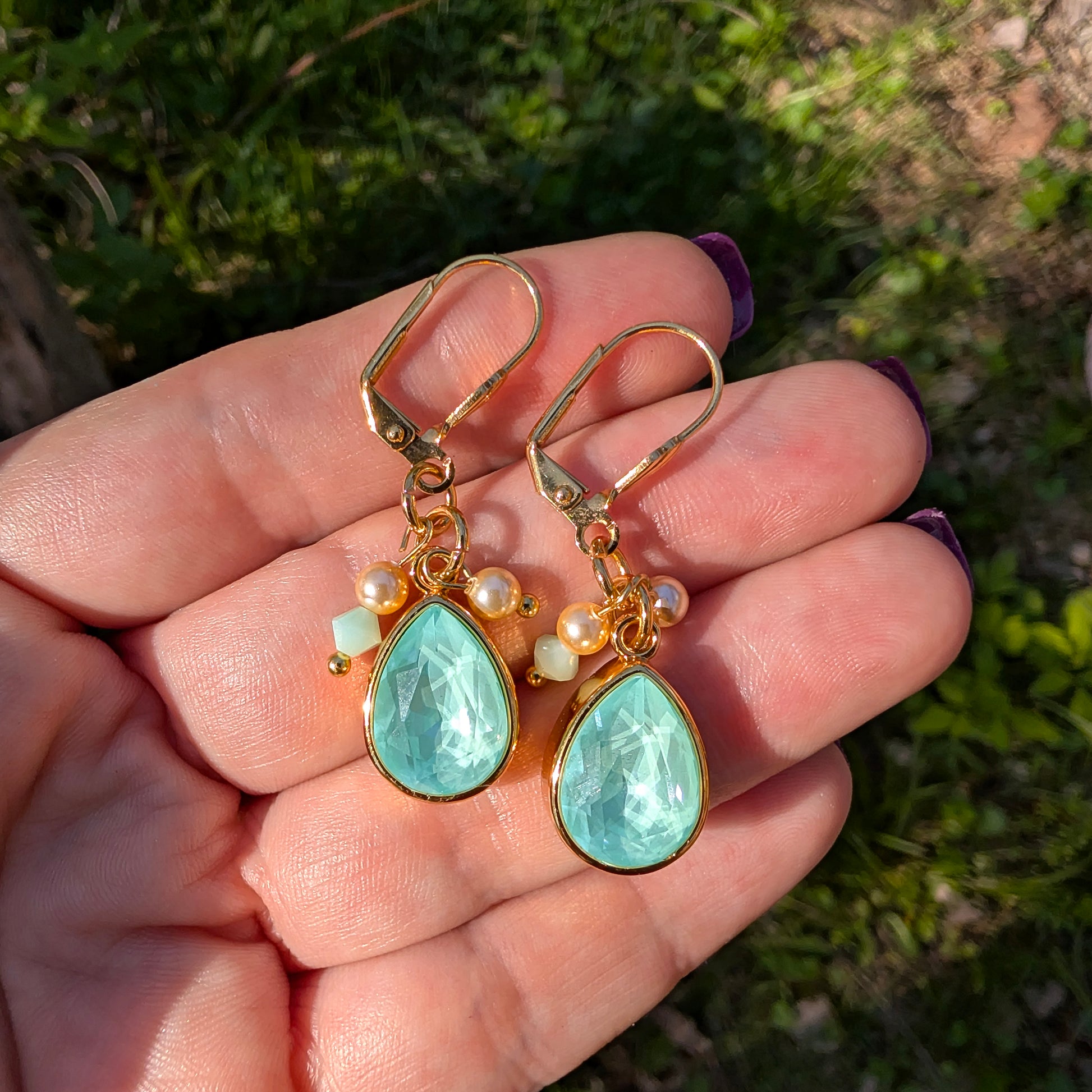 Gold earrings with mint green Swarovski stones held in a hand against a natural background