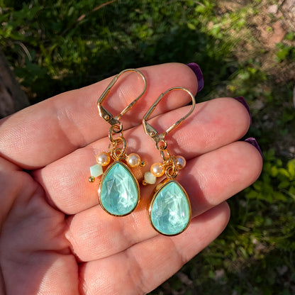 Gold earrings with mint green Swarovski stones held in a hand against a natural background