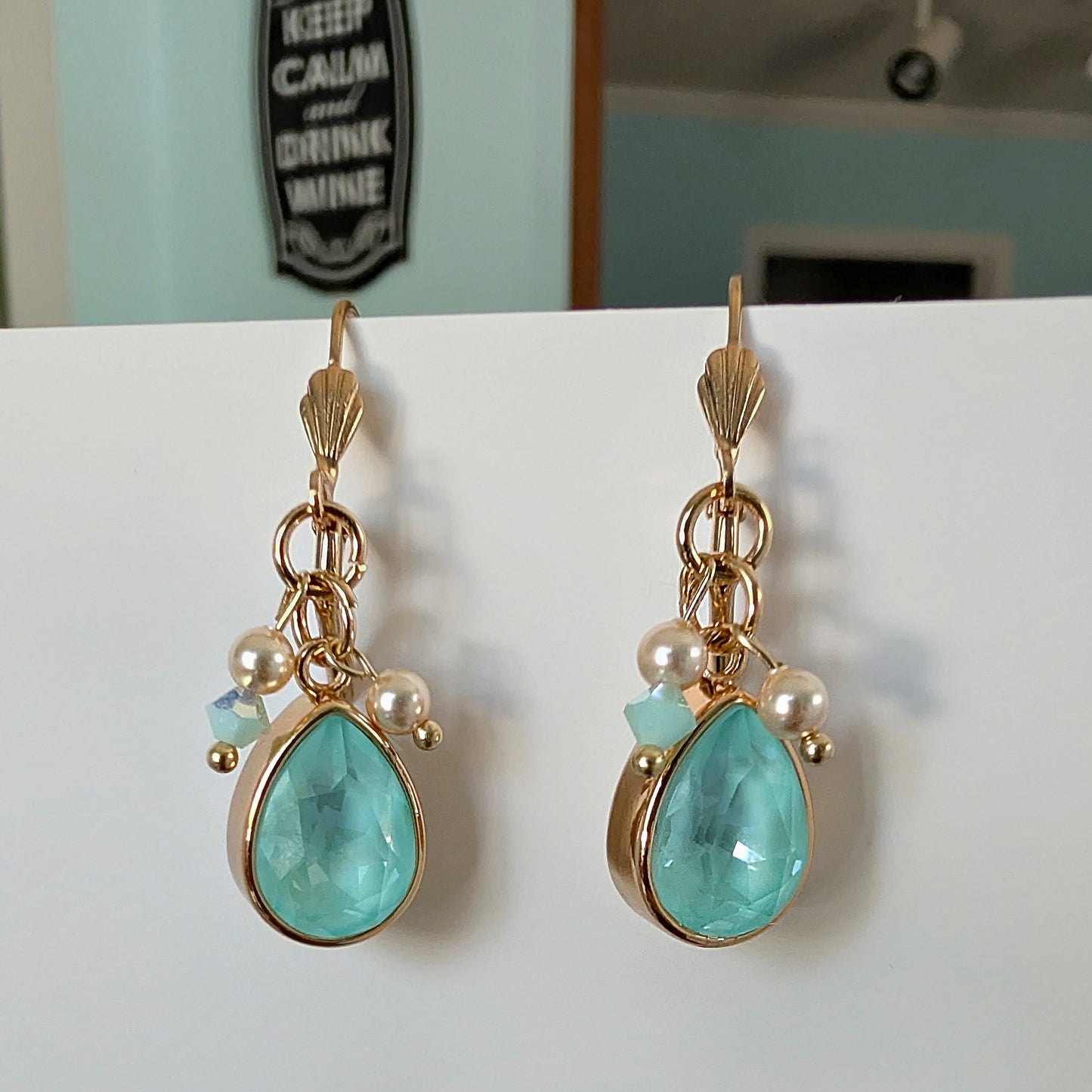Pair of gold earrings with turquoise  mint green teardrop stones and pearls on a white surface.