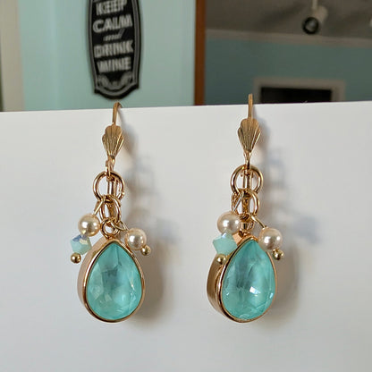 Pair of gold earrings with turquoise  mint green teardrop stones and pearls on a white surface.