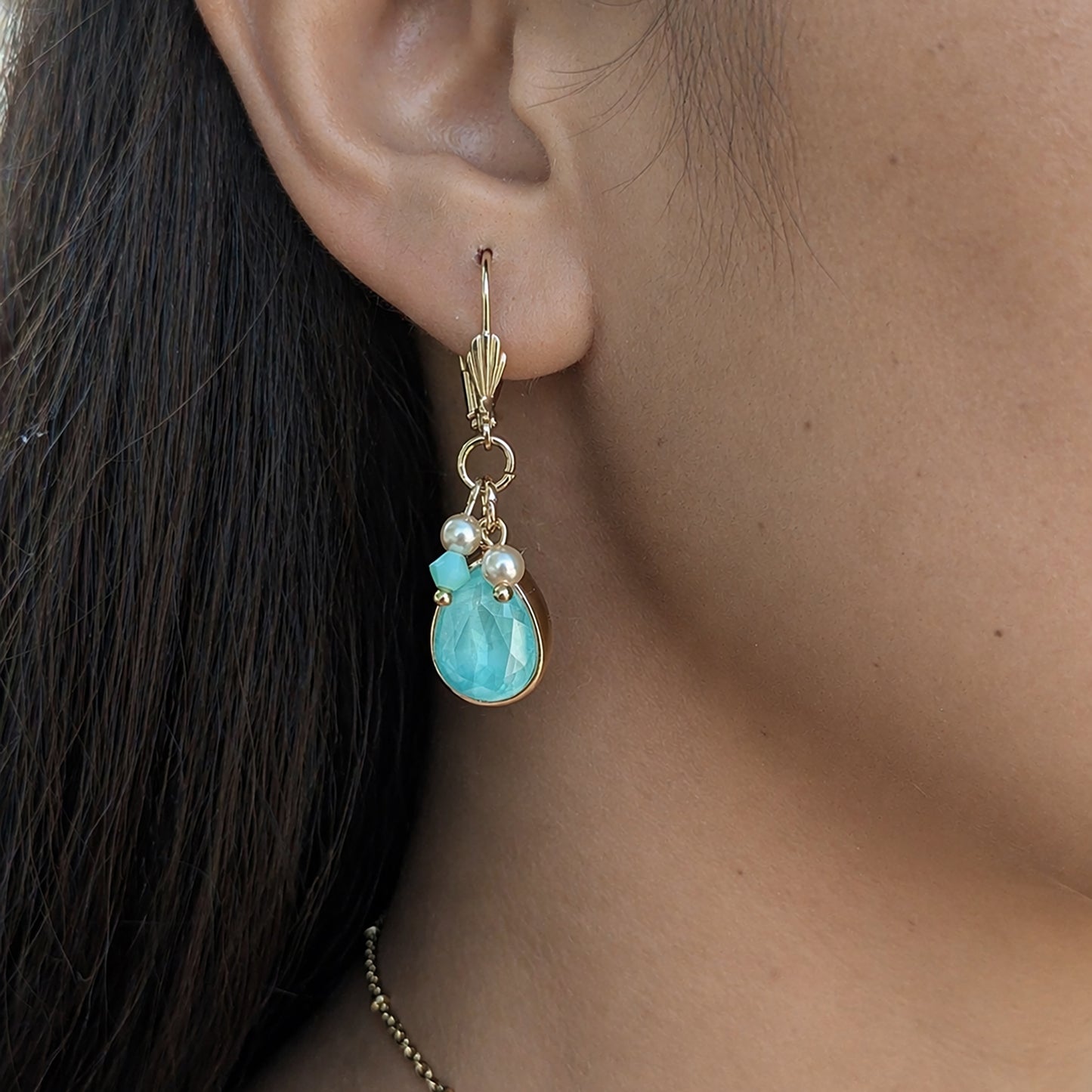 Close-up of an ear wearing a gold earring with a blue teardrop and pearl.