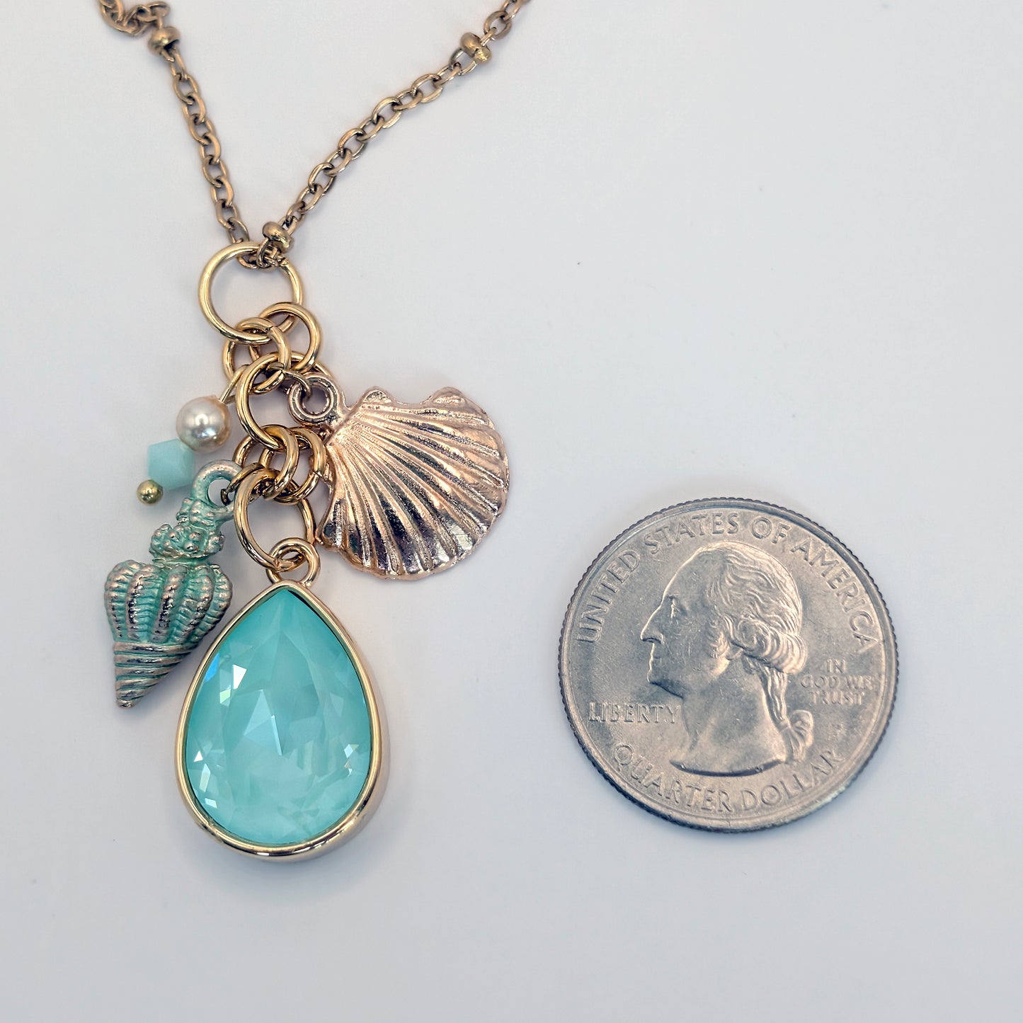 Necklace with a teardrop pendant and shell charms next to a quarter for scale on a white background
