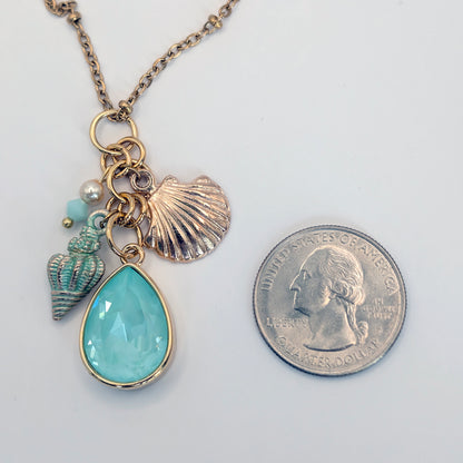 Necklace with a teardrop pendant and shell charms next to a quarter for scale on a white background