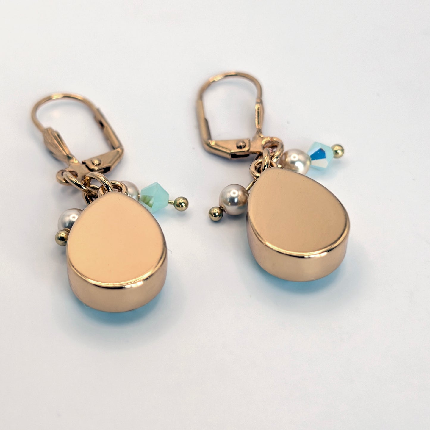 Gold teardrop-shaped earrings with small beads on a light gray background