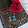 Dragonfly earrings with turquoise stones on a brown fabric background with a red rose.