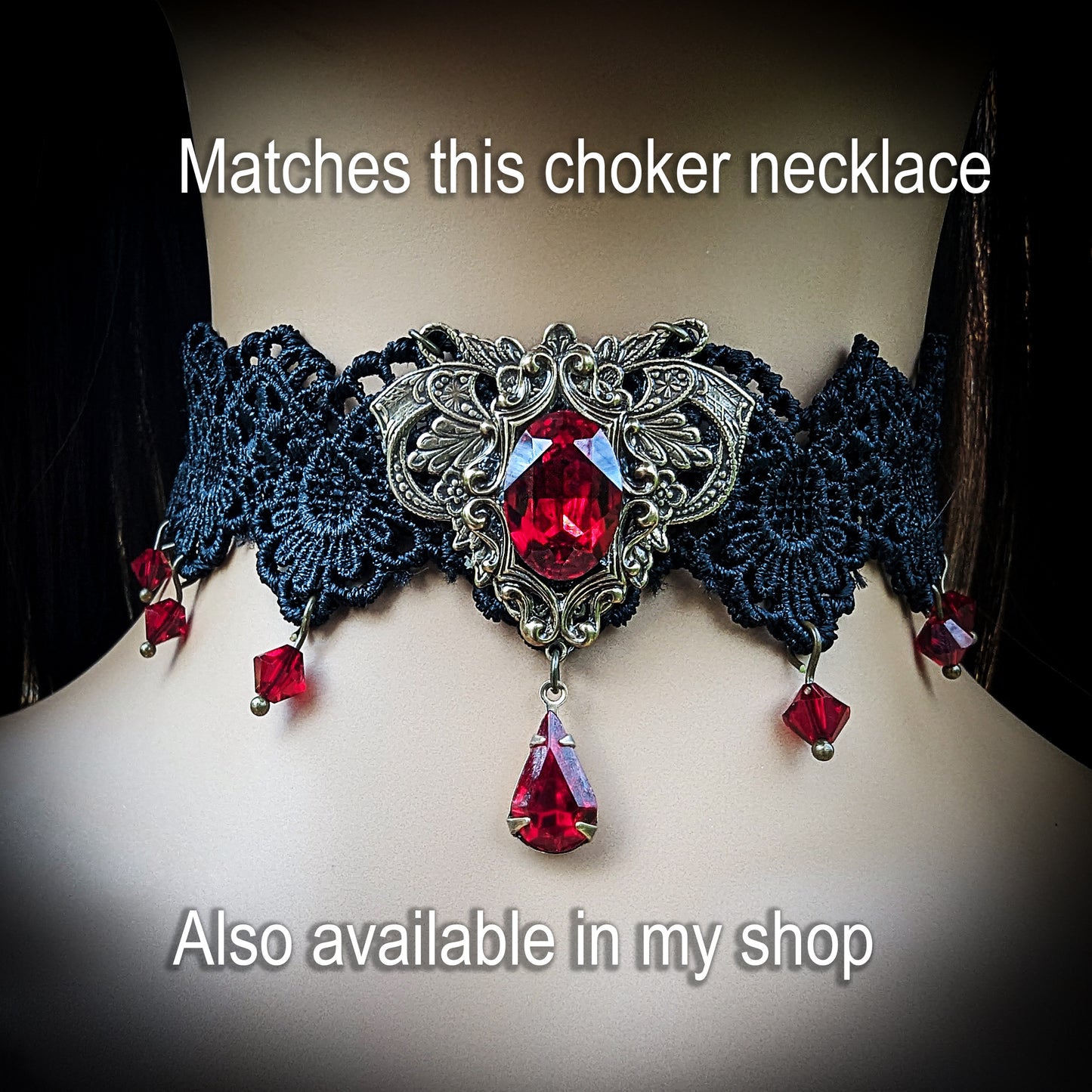 A gothic-style choker necklace displayed on a mannequin bust. The necklace features dark navy blue lace, ornate silver filigree, and large faceted red gemstones, including a central teardrop-shaped red crystal.