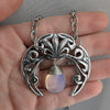 Sterling silver plated Gothic Art Nouveau crescent moon necklace with synthetic blue opal held in hand, without black background.