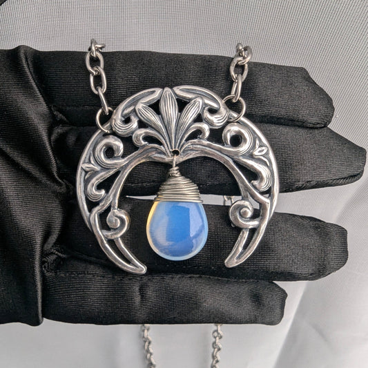 Sterling silver plated Gothic Art Nouveau crescent moon necklace with synthetic blue opal held in hand with black glove.