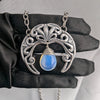 Sterling silver plated Gothic Art Nouveau crescent moon necklace with synthetic blue opal held in hand with black glove.
