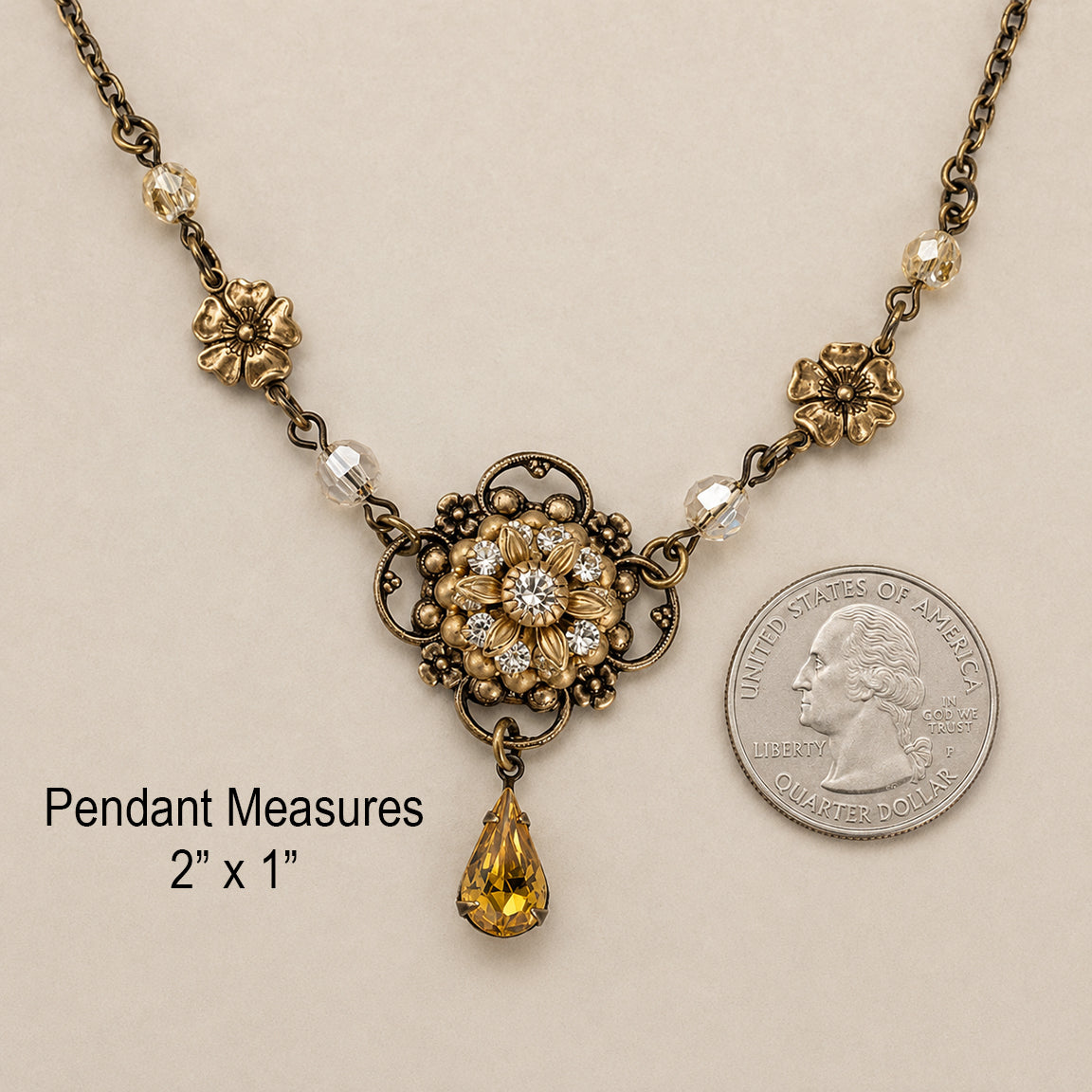 An antique-style flower necklace with a central floral sunflower medallion with crystals, small gold beads, honey faceted beads, and a teardrop-shaped light topaz crystal pendant, displayed on a textured cream background with a quarter for size comparison.