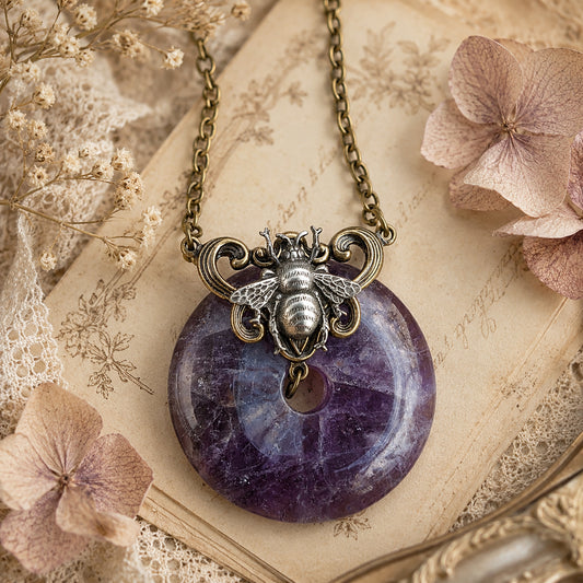 Necklace with natural purple Amethyst donut stone and bee pendant on an old book with flowers.  Boho bee nature inspired jewelry