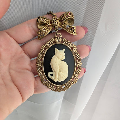 Antique brass-framed pendant with a cat design held by a hand against a white background.  Cat lover jewelry