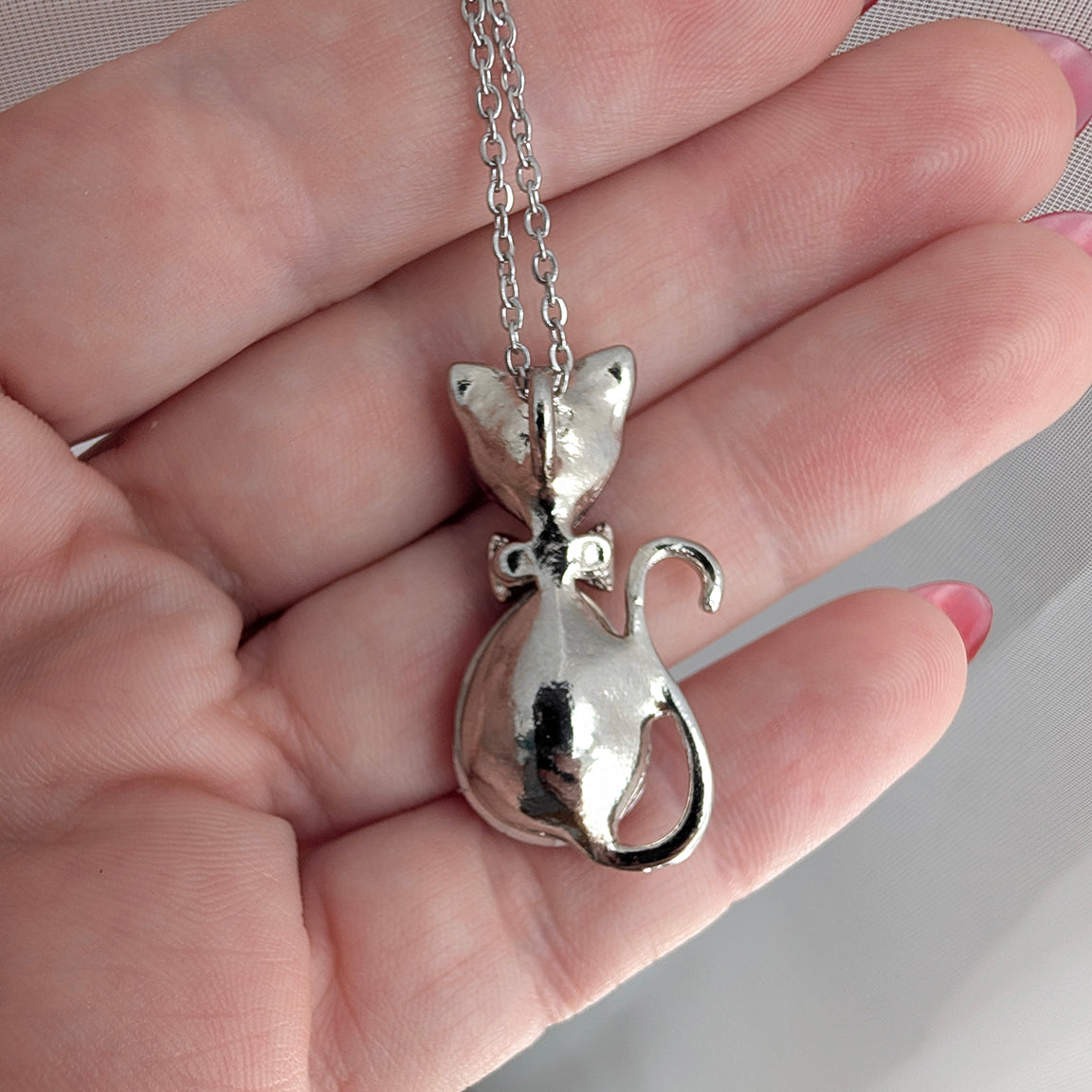 Silver cat-shaped pendant on a chain held in a hand.