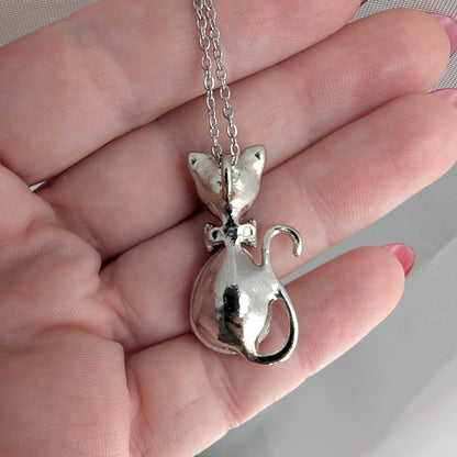 Silver cat-shaped pendant on a chain held in a hand.
