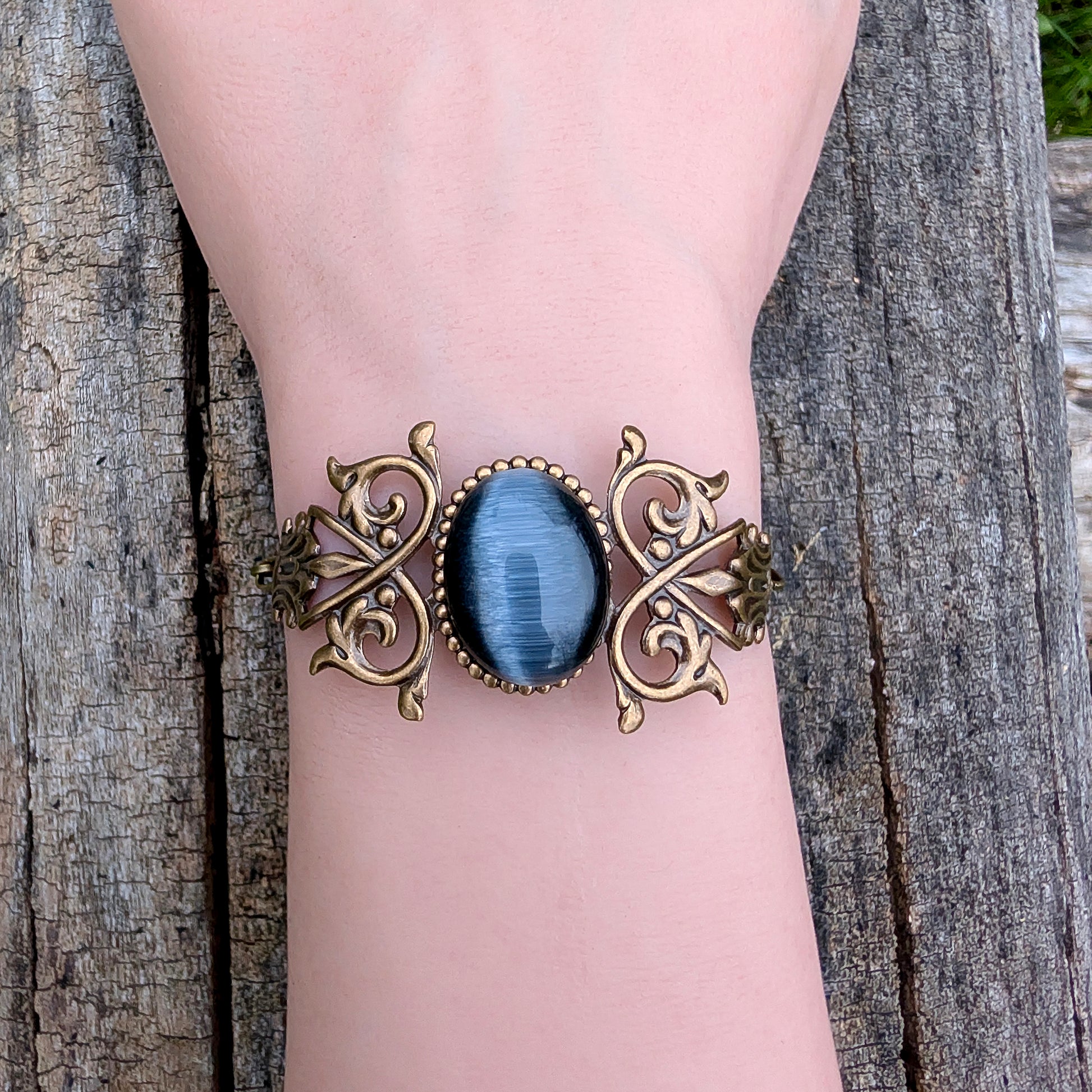 Black cats eye gothic Victorian brass bracelet on a wrist, outside.