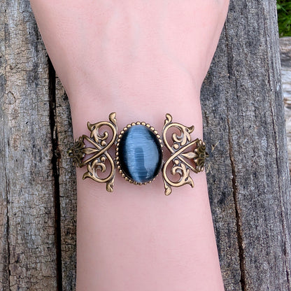 Black cats eye gothic Victorian brass bracelet on a wrist, outside.