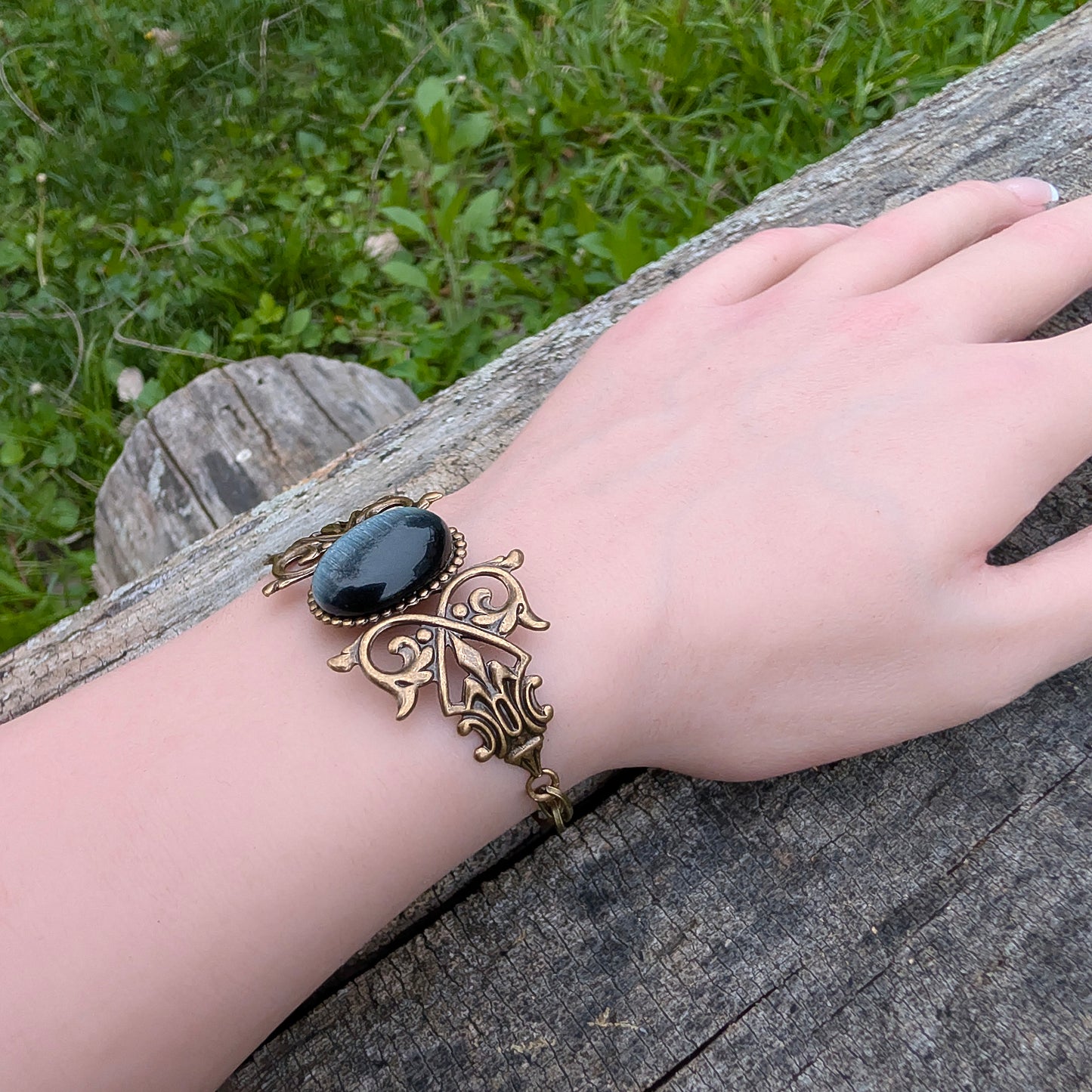 Black cats eye gothic brass bracelet on wrist, outdoors.