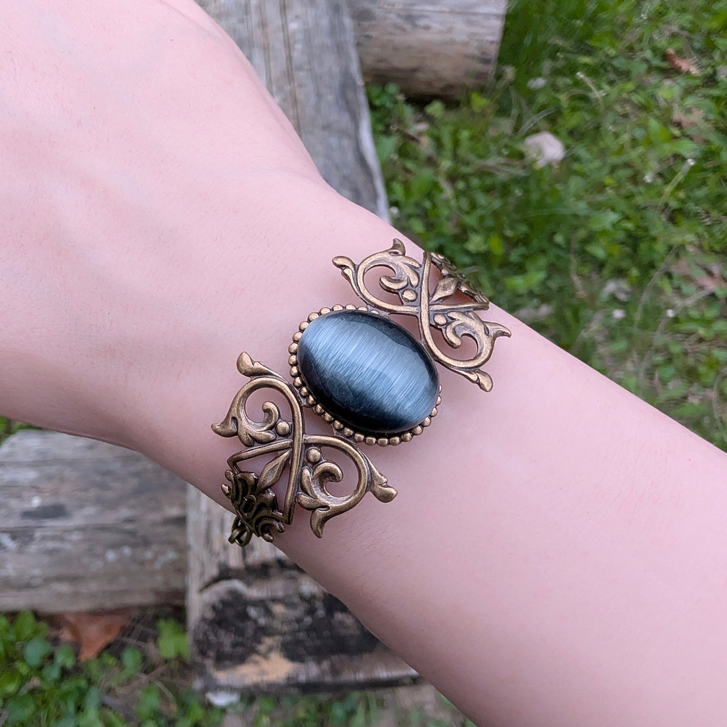 Black cats eye gothic brass bracelet on wrist, outdoors.