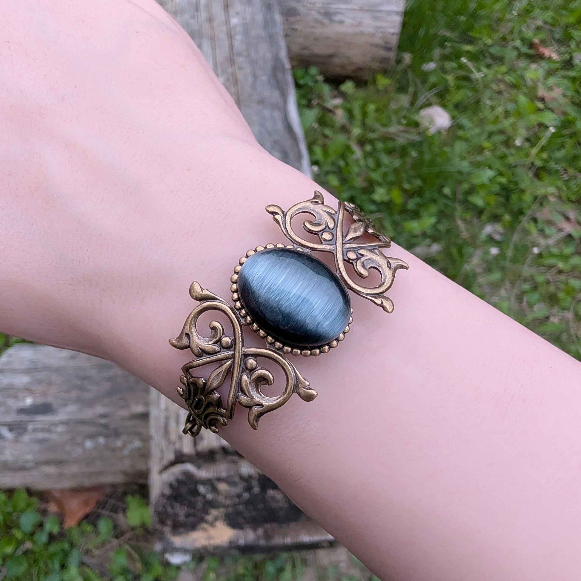 Black cats eye gothic brass bracelet on wrist, outdoors.