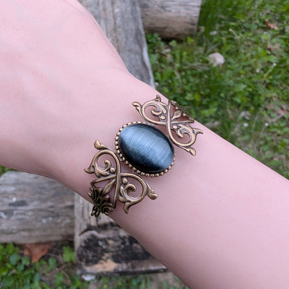 Black cats eye gothic brass bracelet on wrist, outdoors.