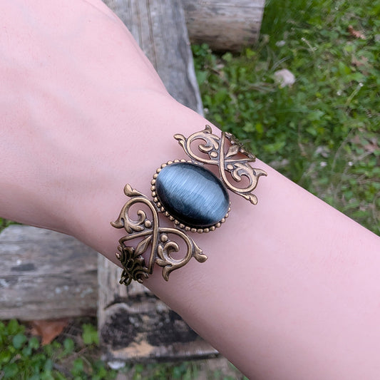 Black cats eye gothic brass bracelet on wrist, outdoors.