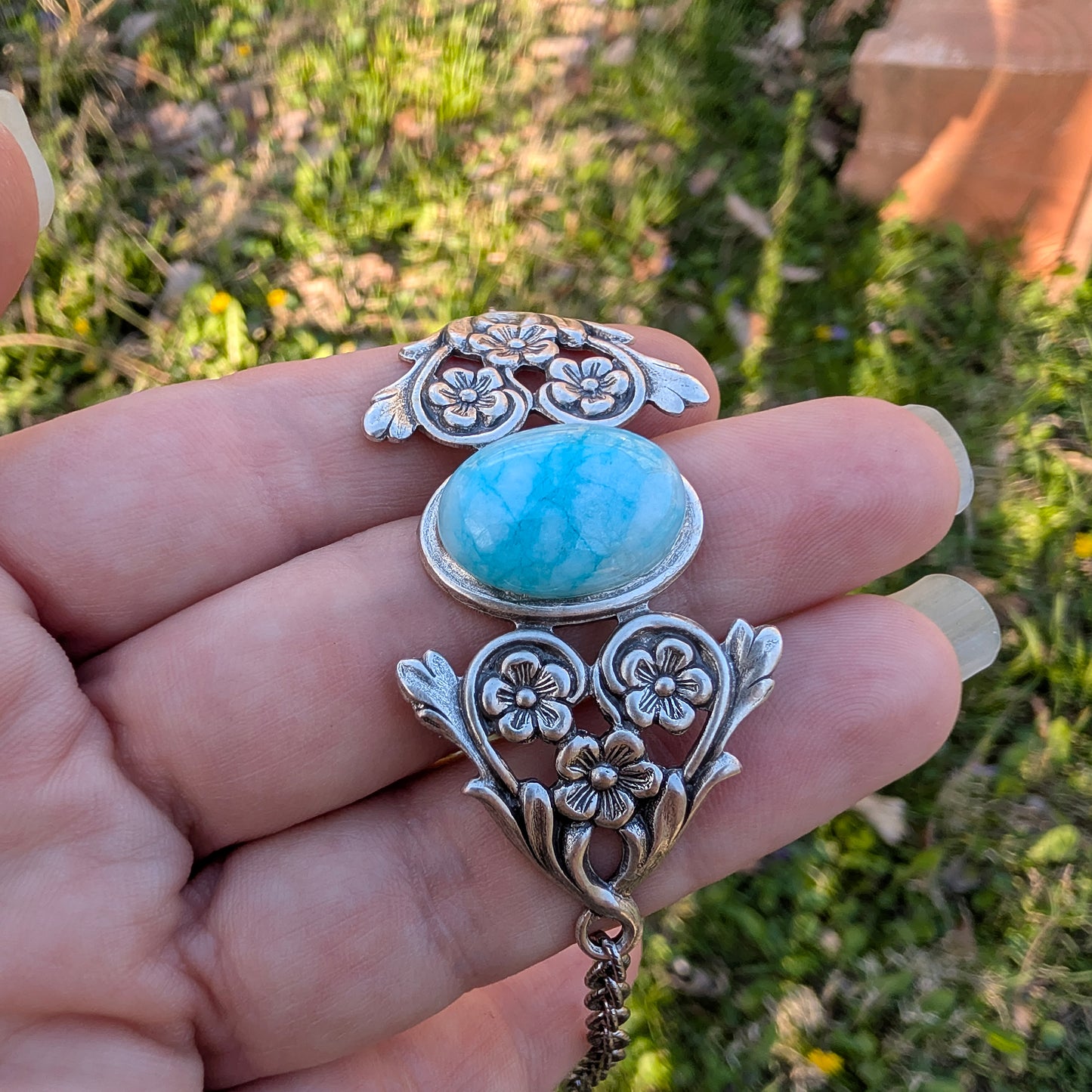 Silver pendant with a blue stone held in a hand against a natural background