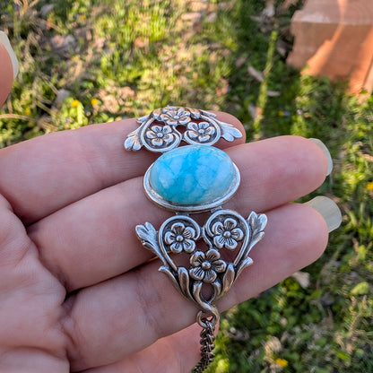 Silver pendant with a blue stone held in a hand against a natural background