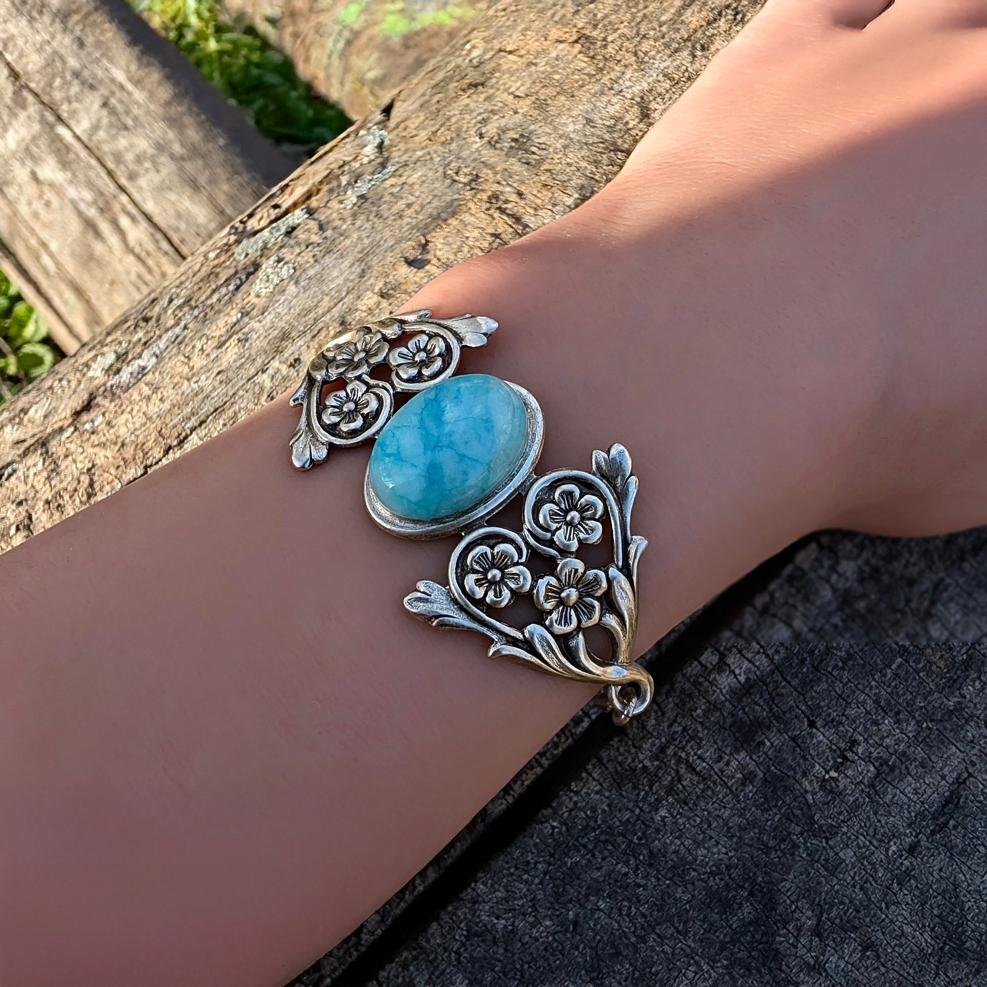 Silver natural Blue Amazonite Ocean stone bracelet with floral detail on a wrist against a natural background