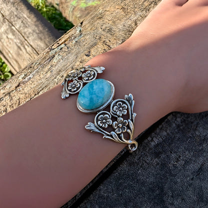 Silver natural Blue Amazonite Ocean stone bracelet with floral detail on a wrist against a natural background