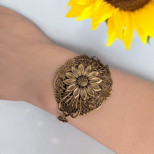 Brass floral bracelet on a wrist with a sunflower in the background