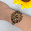 Brass floral bracelet on a wrist with a sunflower in the background