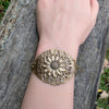 Bronze brass sunflower floral bracelet on a wrist against a wooden background