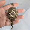 Bronze brass floral sunflower baracelet held between fingers against a neutral background