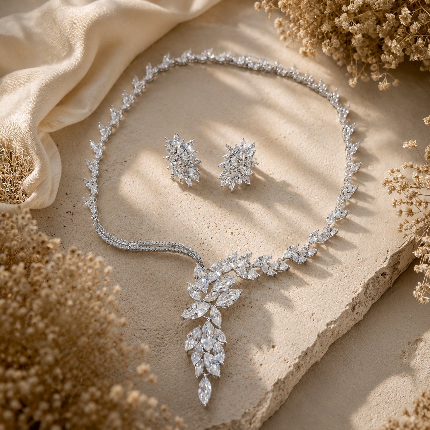 Silver cubic zirconia bridal jewelry set with necklace and earrings on a textured surface with dried flowers.