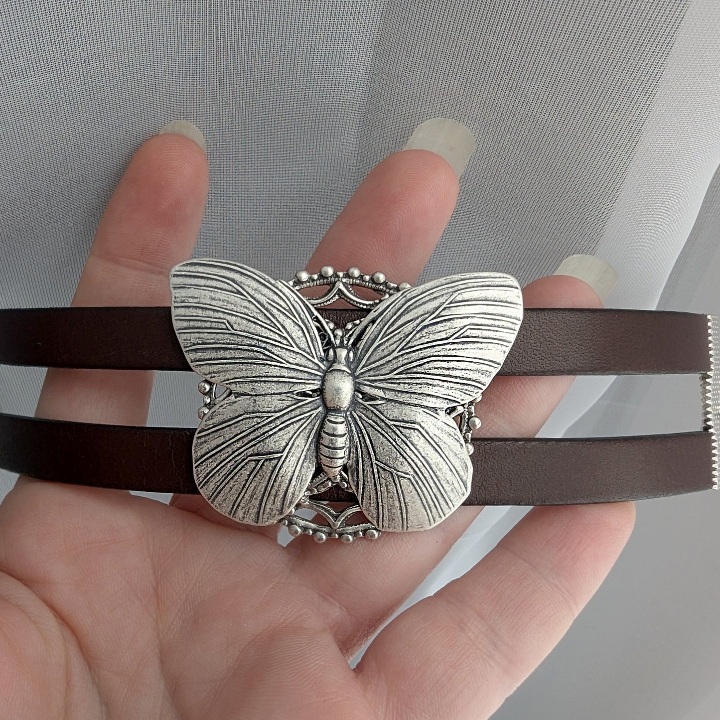 silver Butterfly bracelet on a brown leather strap held by a hand.