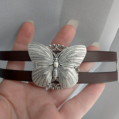 silver Butterfly bracelet on a brown leather strap held by a hand.