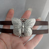 silver Butterfly bracelet on a brown leather strap held by a hand.