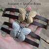 Butterfly-shaped bracelets in silver and brass held in a hand with text 'Available in Silver or Brass'.